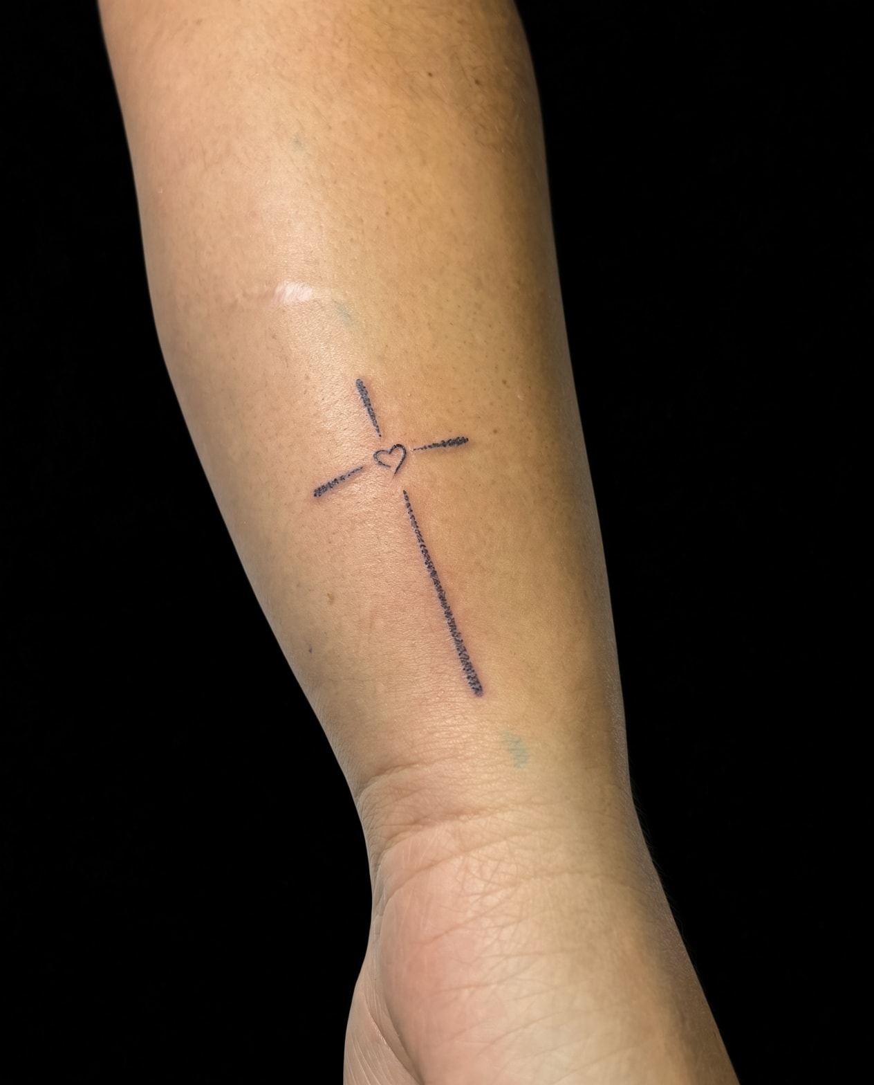 Tatuaje fineline de cruz con corazón en antebrazo