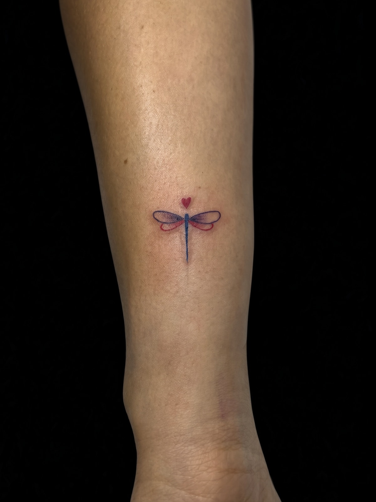 Tatuaje fineline de libélula con corazón en pierna