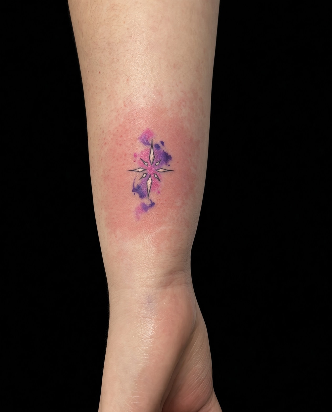 Tatuaje fineline de estrella cruz con acuarela en muñeca