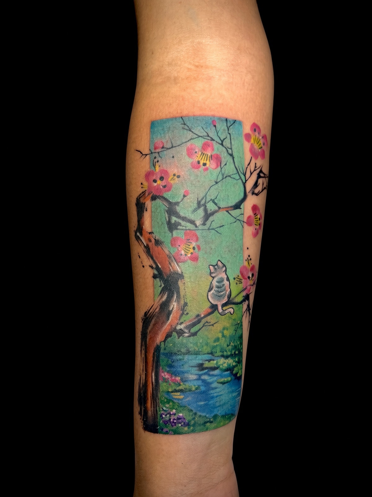 Tatuaje estilo libre de gato en árbol de cerezo con paisaje a color en el antebrazo