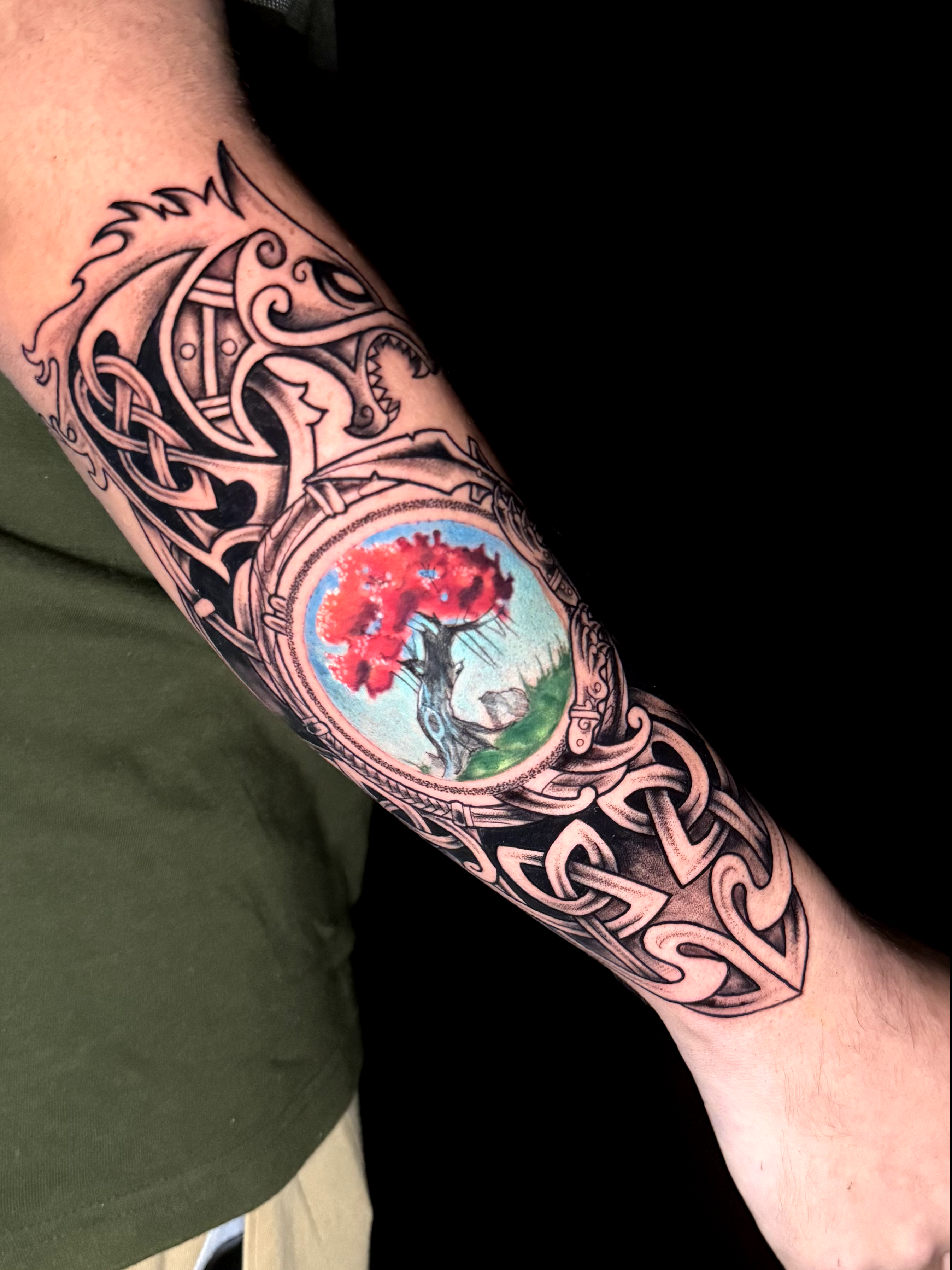 Tatuaje estilo libre de fusión celta y maorí con árbol a color en el antebrazo