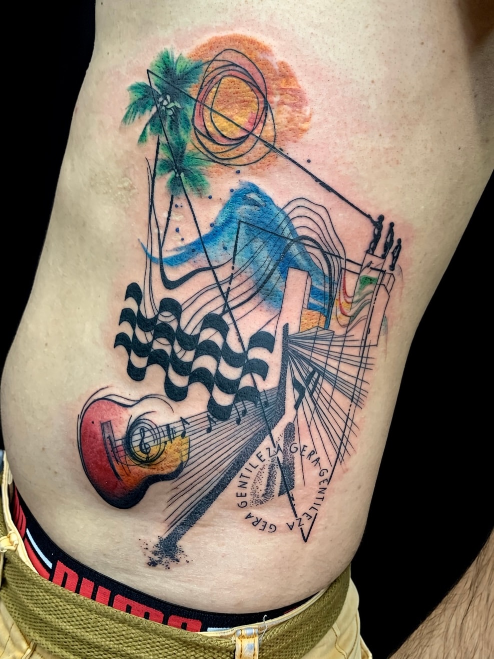 Tatuaje estilo libre de guitarra, olas y palma en las costillas