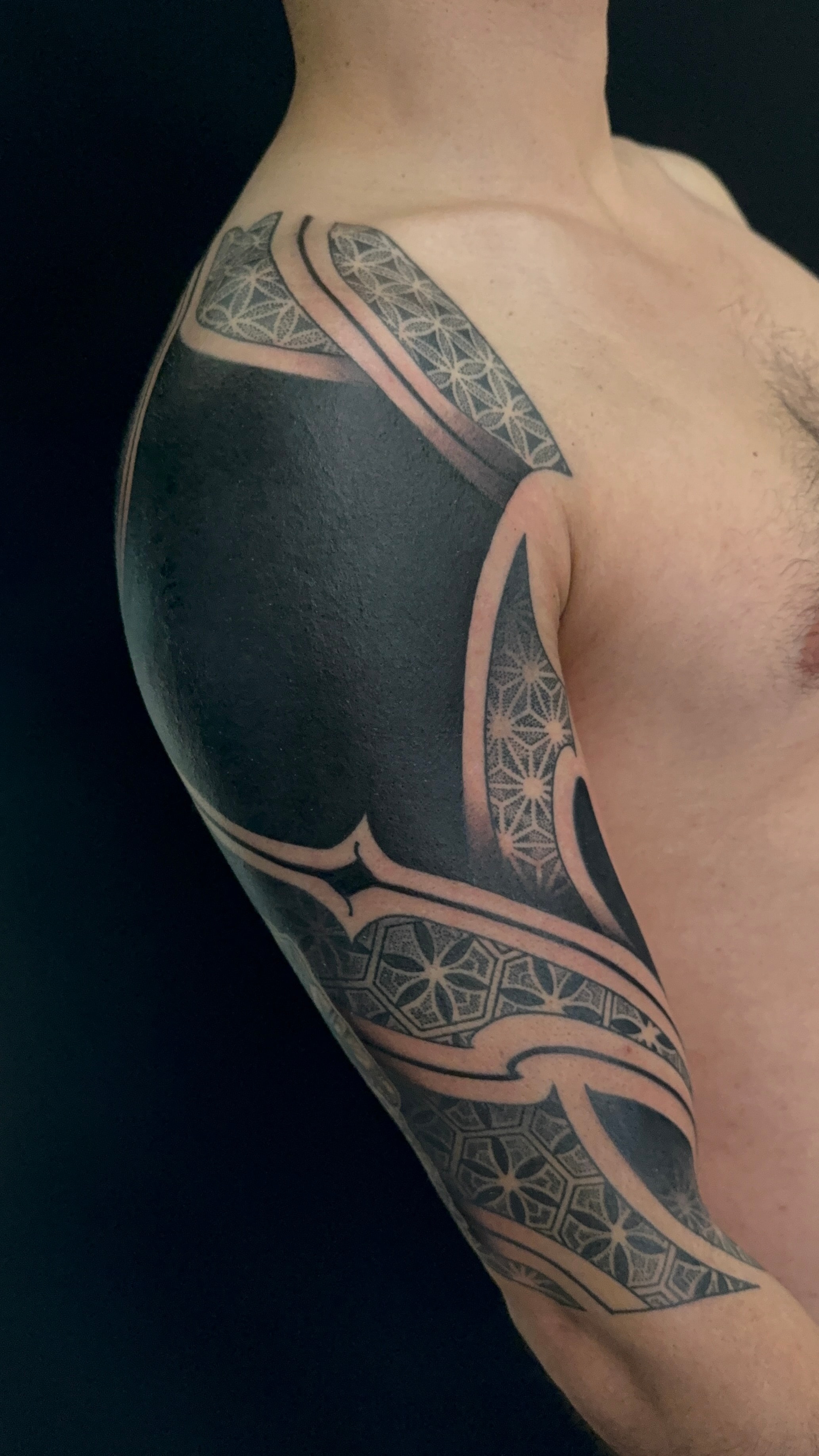 Tatuaje blackout geométrico en hombro y brazo