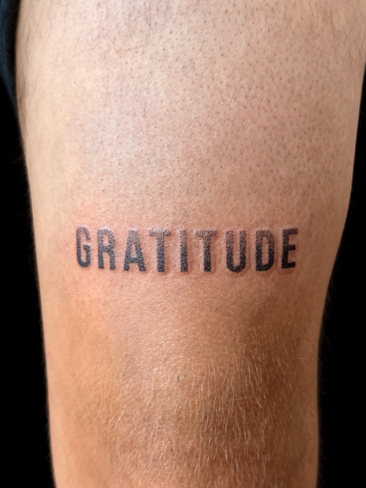 Tatuaje lettering GRATITUDE en tipografía de bloque en muslo