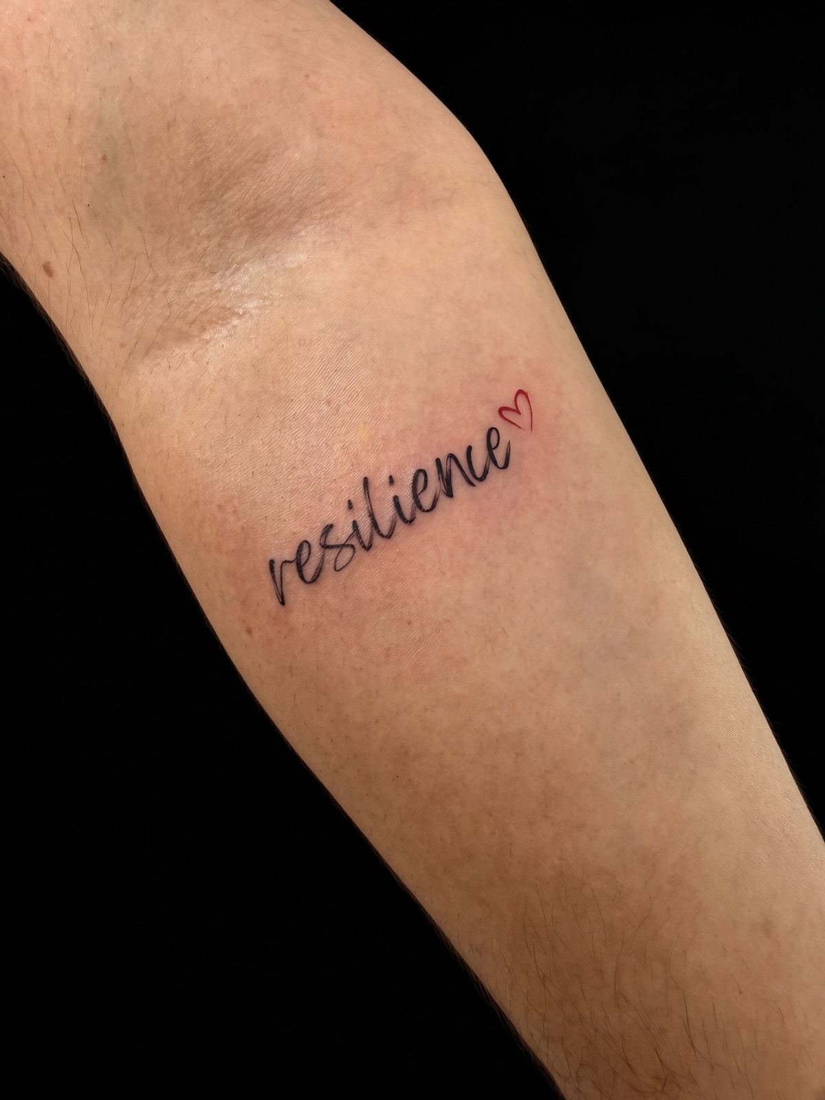 Tatuaje lettering resilience con corazón rojo en antebrazo