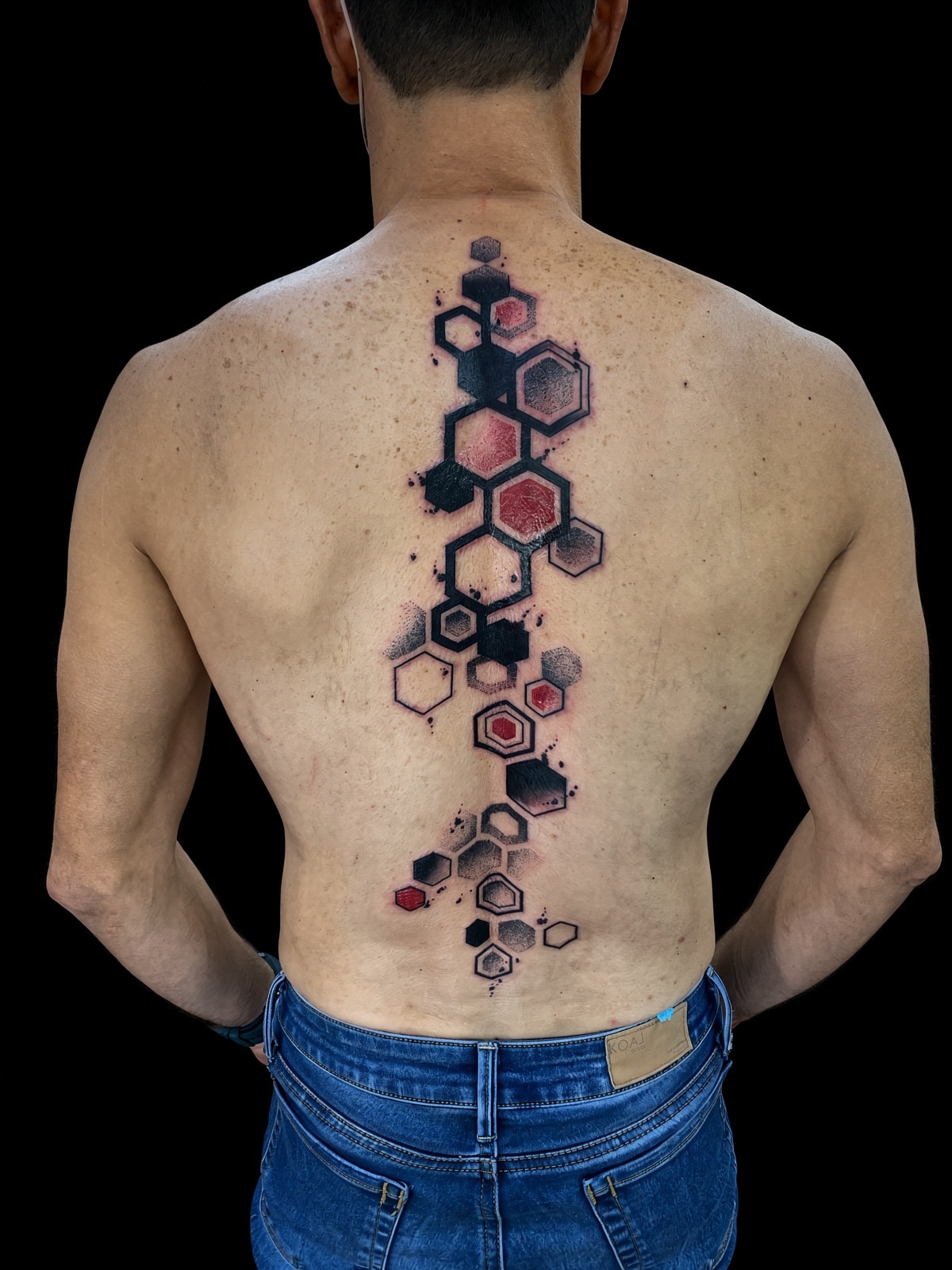 Tatuaje trash polka de hexágonos en rojo y negro en la espalda completa
